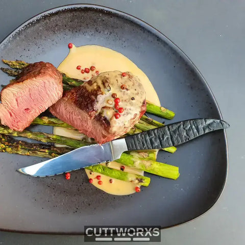 Medium-rare Steak mit Spargel und cremiger Sauce auf dunklem Teller für Messerarten in der Küche