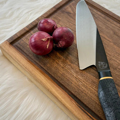 Schwarzer Griffkochenmesser auf Nussbaum Massivholz Steak-Brett mit roten Zwiebeln