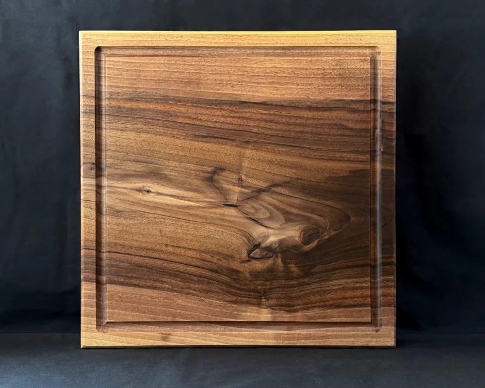 Massives Nussbaum-Schneidebrett 50 × 50 × 5 cm in frontaler Vorderansicht mit Saftrille und markanter natürlicher Holzmaserung